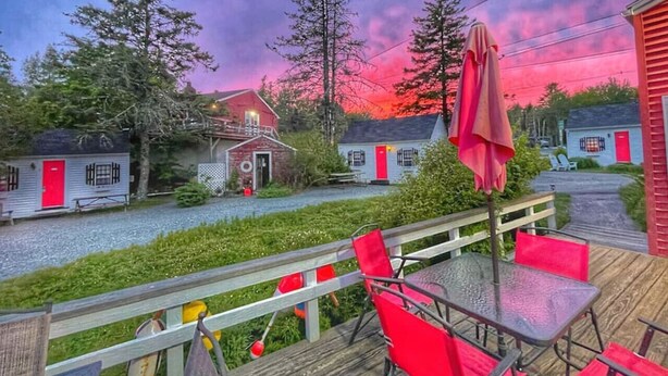Una terraza con sillas rojas y una mesa, con vista a un pueblo con casas pequeñas y un puente de madera.