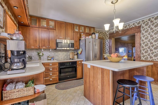 A kitchen with wooden cabinets, a microwave, a refrigerator, a coffee maker, and a central island with stools. - Open Hearth Inn Cottage 8 - 10 min to Acadia! (Trenton)