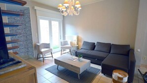Ein modernes Wohnzimmer mit einem grauen Sofa, einem weißen Couchtisch und einer Chandelieber. Eine Ziegelwand und ein großes Fenster sind ebenfalls vorhanden.
