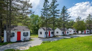 A row of small, white cabins with red doors, each with a picnic table in front.