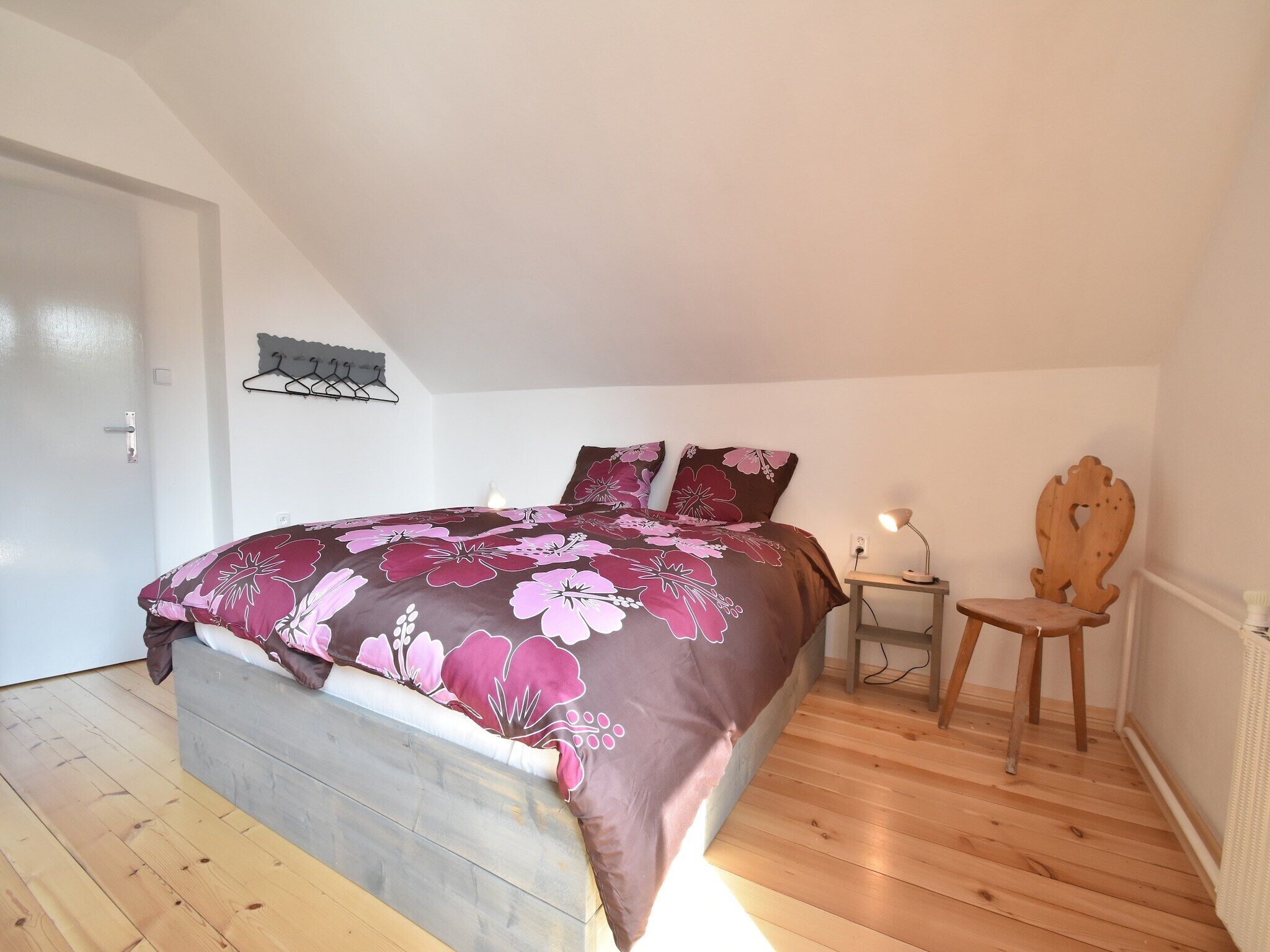 A bedroom with a bed, a chair, a nightstand, and a wall-mounted lamp.