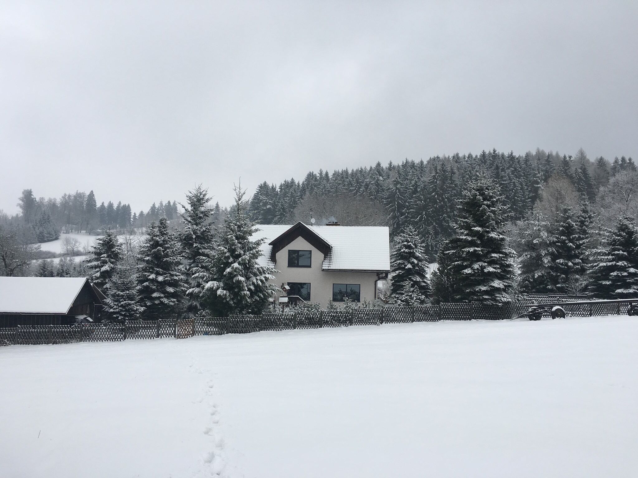 Une maison avec un toit en pente, entourée d’arbres couverts de neige et d’une clôture.