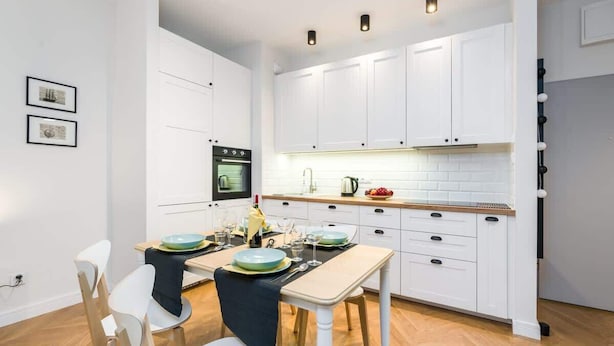 A modern kitchen with white cabinets, a built-in oven, and a dining area with a table set for two.