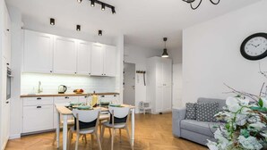 A modern kitchen with white cabinets, a dining table with chairs, and a grey sofa in the living area.