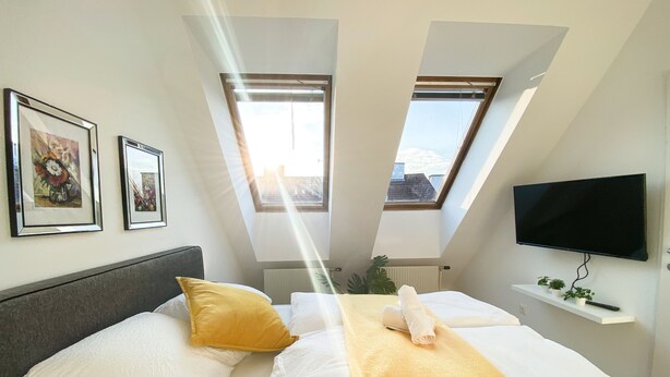 A modern bedroom with a bed, two skylights, a flat-screen TV, and framed pictures on the wall. - Hauptbahnhof Boutique Rooms - Virtual Reception & Self-Checkin (Vienna)