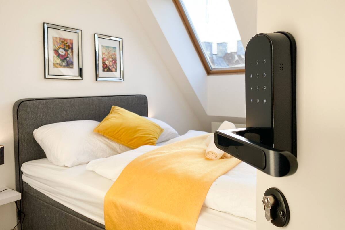 A modern hotel room with a bed, a mounted digital lock, and two framed artworks on the wall.
