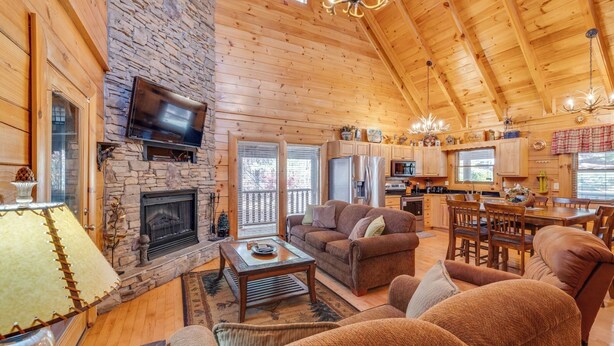 A cozy log cabin interior with a stone fireplace, wooden furniture, and a dining area. - Enchanted Forest - Seasonal Mountain Views, Community Pool & Hot Tub (Sevierville)