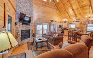 A cozy log cabin interior with a stone fireplace, wooden furniture, and a dining area.
