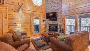 A cozy cabin interior with wooden walls, a stone fireplace, a mounted television, and a comfortable seating area. - Enchanted Forest - Seasonal Mountain Views, Community Pool & Hot Tub (Sevierville)