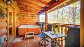 A wooden cabin with a hot tub, a table with chairs, and a view of the forest. - Enchanted Forest - Seasonal Mountain Views, Community Pool & Hot Tub (Sevierville)
