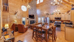 A log cabin interior with a dining area, kitchen, fireplace, and stone accents. - Enchanted Forest - Seasonal Mountain Views, Community Pool & Hot Tub (Sevierville)