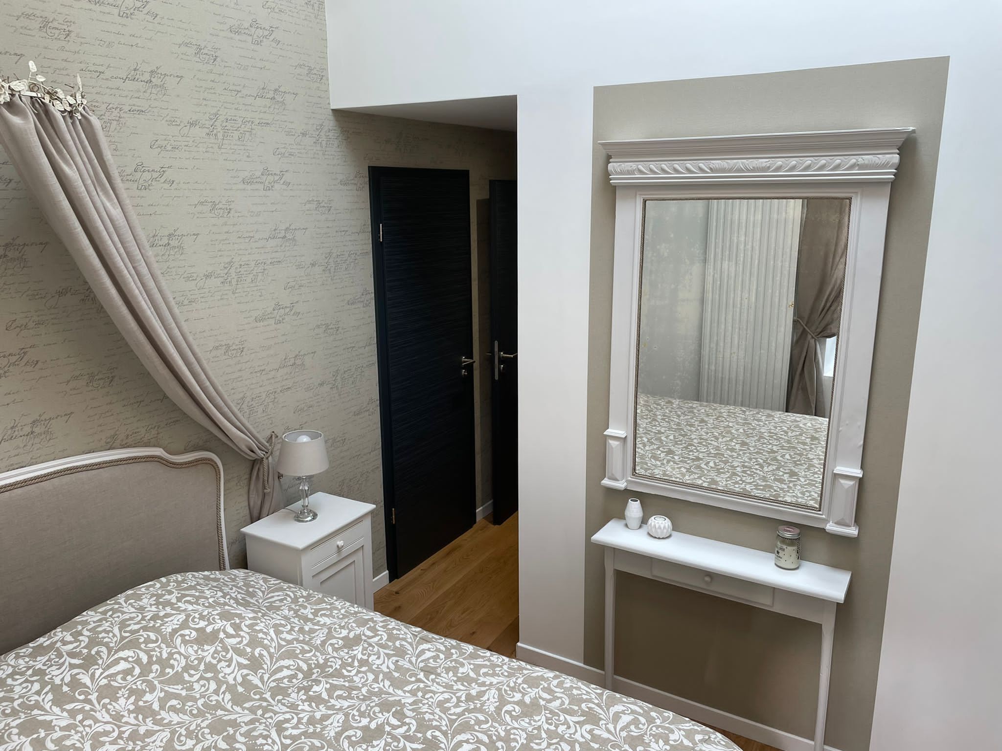 A bedroom with a bed, a bedside table with a lamp, a mirror, and a wardrobe.