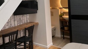Un interior moderno con una escalera, una zona de comedor con mesa y sillas de madera, un baño con lavamanos e inodoro, y una puerta corrediza.