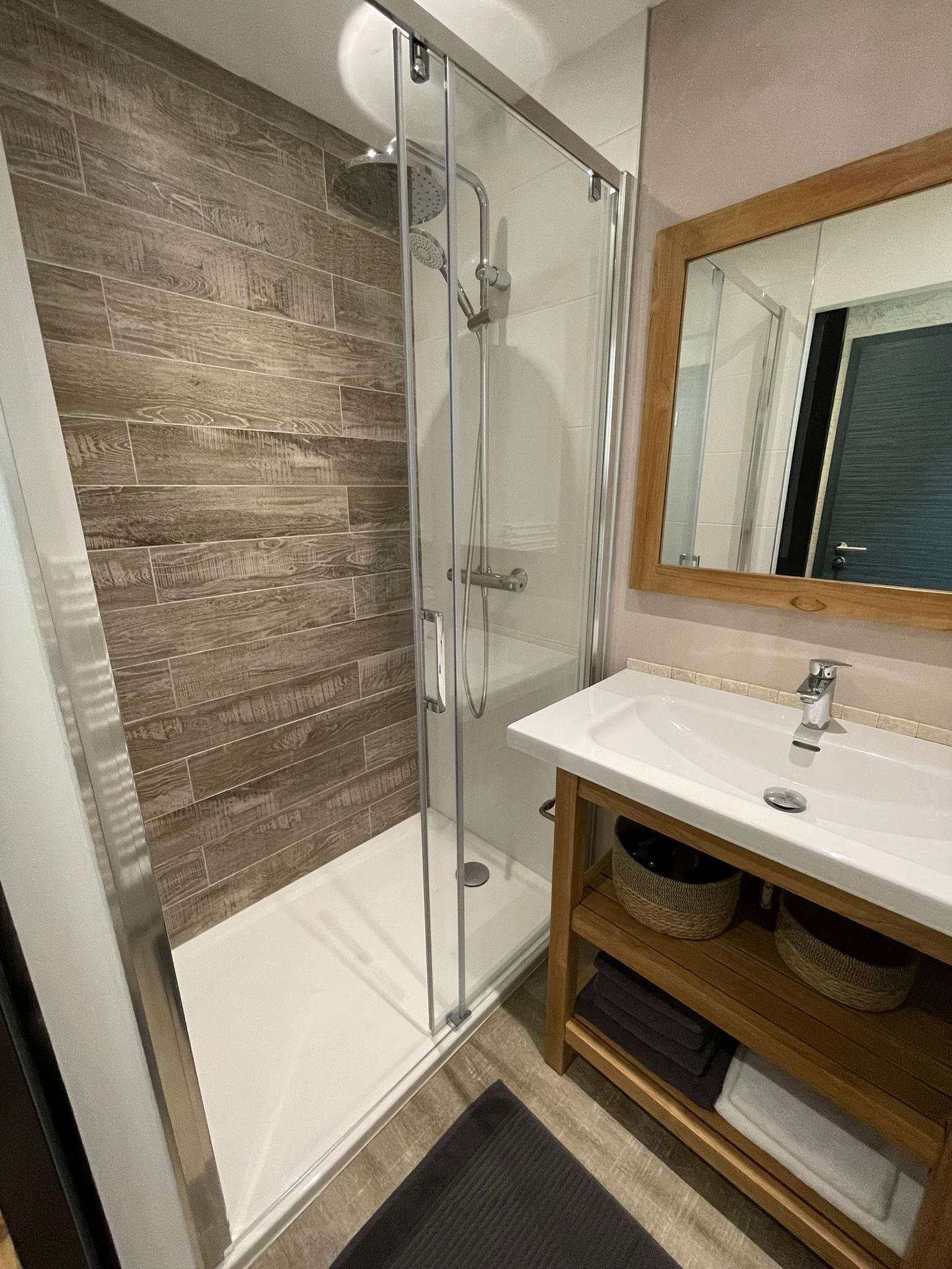 A modern bathroom with a glass-enclosed shower, a white sink, and a wooden vanity.
