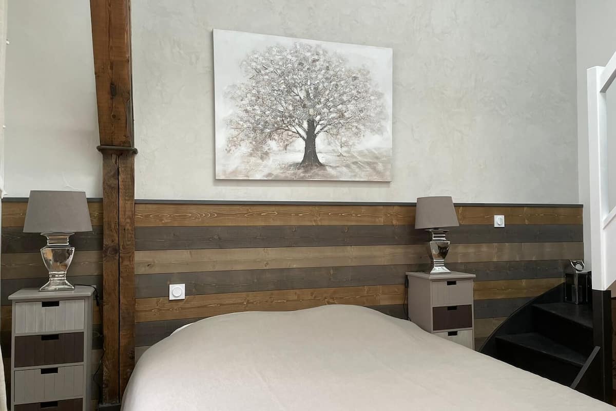 Une chambre à coucher comprenant un lit, une tête de lit en bois, deux tables de chevet et une lampe fixée au mur.
