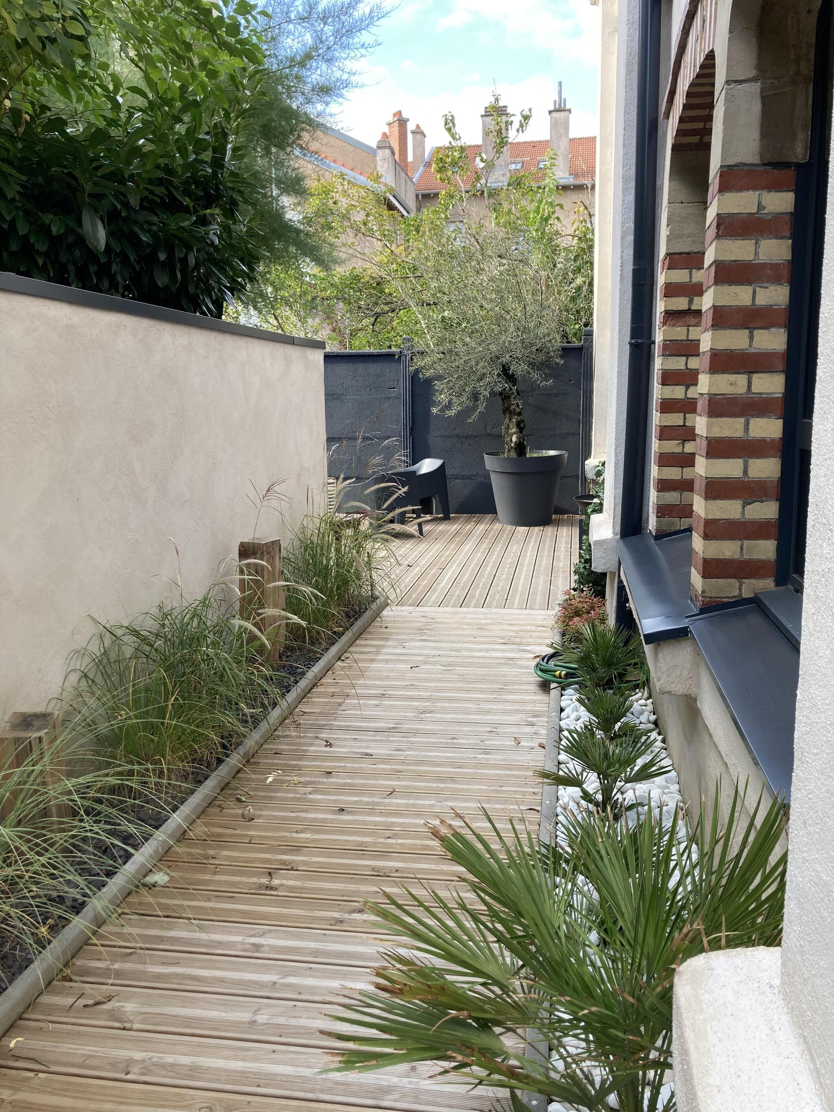 Un estrecho sendero de madera que conduce a un patio con una maceta y una silla.