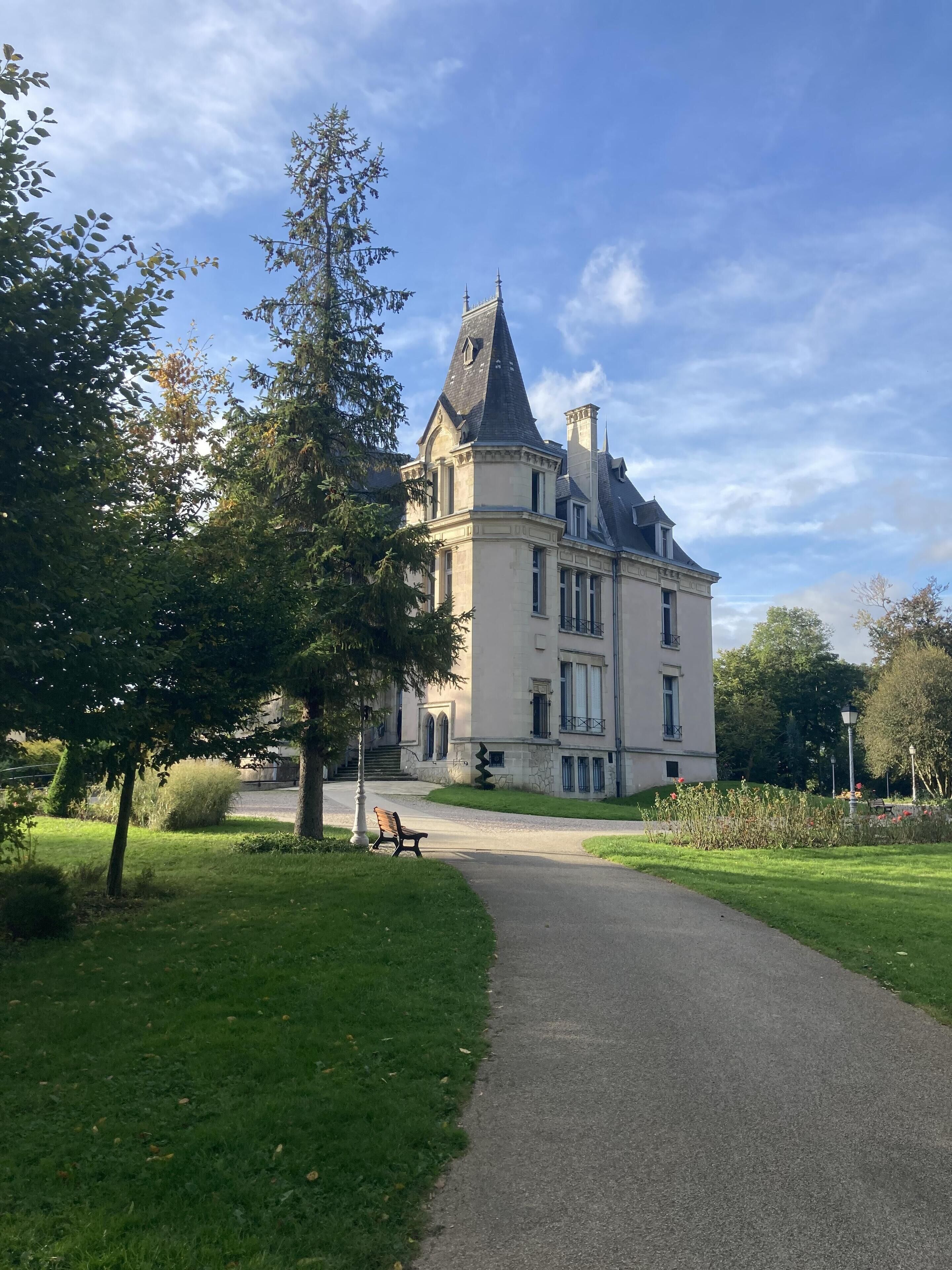 Un grand bâtiment historique, doté d’une tour imposante et d’un jardin bien entretenu, avec un chemin qui y mène.