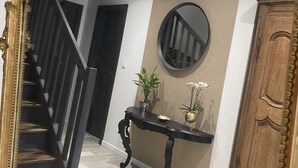 Una escalera con barandillas negras, un espejo redondo en la pared, un armario de madera y una consola decorada con plantas.