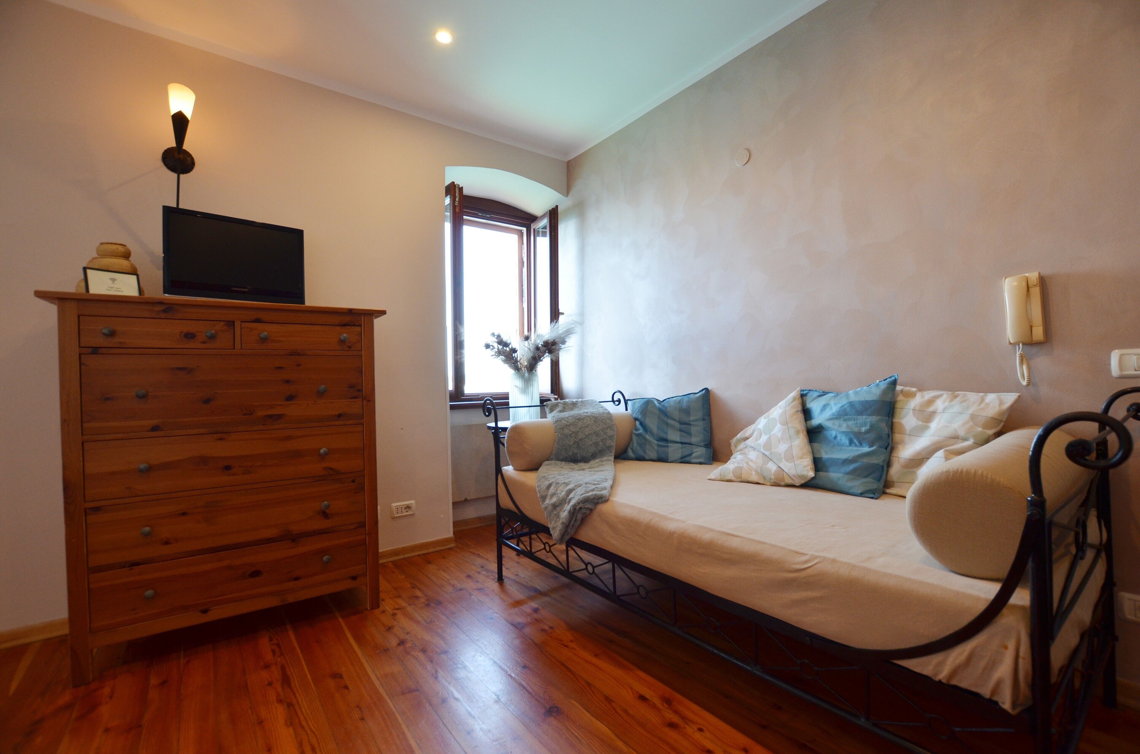 Une chambre à coucher avec une commode en bois, un lit avec plusieurs oreillers, une lampe de chevet et une fenêtre avec des rideaux.