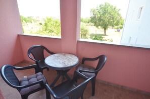 A balcony with a round table and four chairs, a pink wall, and a view of greenery and a building.