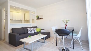 Een moderne woonkamer met een grijze bank, een witte salontafel en een eethoek met een witte tafel en stoelen.