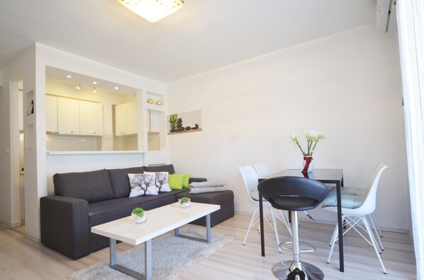 A modern living room with a grey sofa, a white coffee table, and a dining area with a white table and chairs.