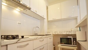 Een moderne keuken met witte kastjes, een marmeren aanrecht, een roestvrijstalen spoelbak en een magnetron op een tafeltje.
