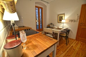 Una cocina compacta con mostradores de madera, una mesa de comedor y sillas. Se observa una ventana con vistas a árboles, una puerta y un teléfono instalado en la pared.