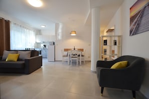 A modern living room with a sofa and armchair, a dining area with a table and chairs, and a kitchen in the background. - Irene modern apartment (Rovinj)