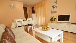 Een woonkamer met een bank, een eettafel met stoelen, een televisie en een schaal fruit.