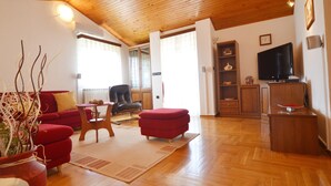 Een ruime woonkamer met een houten plafond, rode banken, een houten salontafel en een televisie.