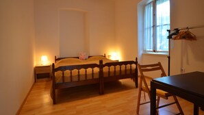 Ein Schlafzimmer mit einem hölzernen Bett, Nachttischen mit Lampen, einem Fenster mit Vorhängen sowie einem Tisch mit Stühlen.