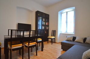 A living room with a sofa, a dining table with chairs, a bookshelf, and a television.