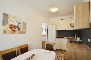 Uma cozinha compacta com armários de madeira, uma geladeira e um fogão. Há uma mesa de jantar com cadeiras e um quadro na parede.