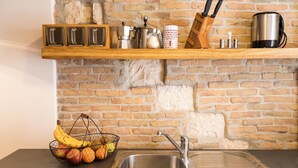 Eine Küche mit Backsteinwand, Spüle aus Edelstahl, einer Holzauslage mit Küchenutensilien und einem Obstkorb.