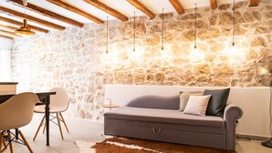 Ein gemütliches Zimmer mit einer Steinwand, einem grauen Sofa, einer Holzbalkendecke und Pendelleuchten.