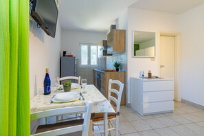 A compact kitchen with a dining area, a TV mounted on the wall, and a small cabinet with a mirror. - Cuvi Beach - Park Studio (Rovinj)