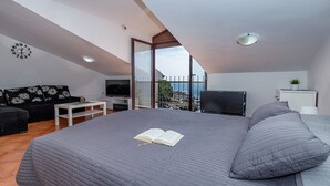 A bedroom with a large bed, a TV, a sofa, and a balcony with a view. - Cuvi Beach - Mansarde Apartment (Rovinj)