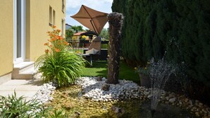 A garden with a water feature, a patio with outdoor furniture, and a tall coniferous tree. - Parenzo Green Garden (Porec)
