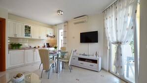 A modern kitchen with white cabinets, a glass dining table, and a flat-screen TV mounted on the wall. - Parenzo Green Garden (Porec)