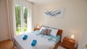 A neatly made bed with blue towels, a wooden nightstand with a lamp, and a painting on the wall. - Parenzo Green Garden (Porec)
