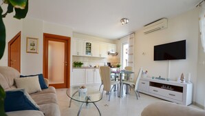 A modern living room with a glass coffee table, a sofa, a dining area with a glass table, and a kitchen with white cabinets and a flat-screen TV. - Parenzo Green Garden (Porec)