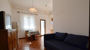 A living room with a sofa, a television on a cabinet, a dining table with a tablecloth, and a patterned ceiling light. - Orbanic Valalta Apartment 1 (Rovinj)