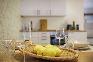 A kitchen with a wicker basket containing lemons, a wine glass, and a glass on a wooden table.