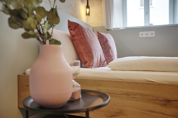 A cozy room with a bed, a bedside table with a vase, and a window with a view.
