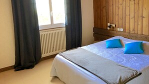 Ein Zimmer mit einem Bett, einem Vorhangfenster, einem Heizkörper und Holzwandverkleidung.