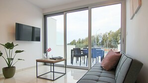 Una sala de estar moderna con un sofá gris, una mesita, una planta en maceta y un televisor montado en la pared.