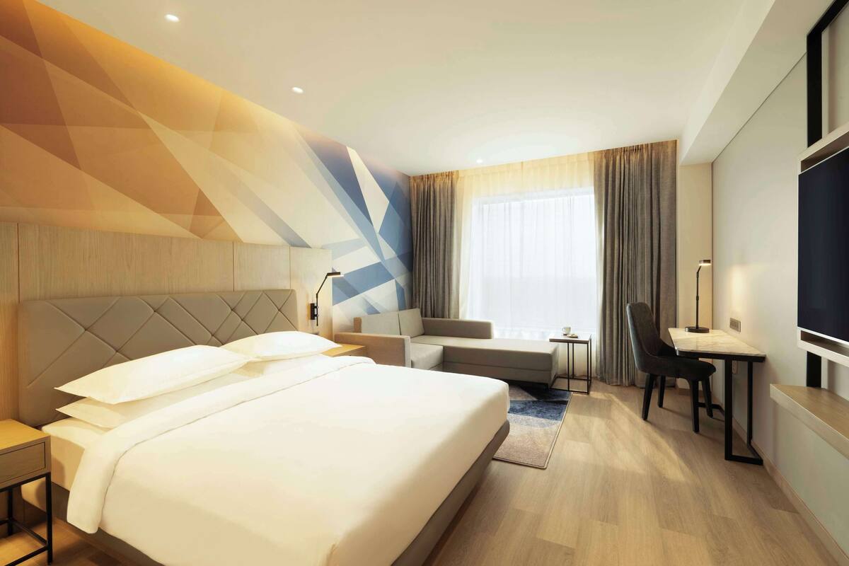 A modern hotel room with a large bed, a sofa, a desk, and a TV.