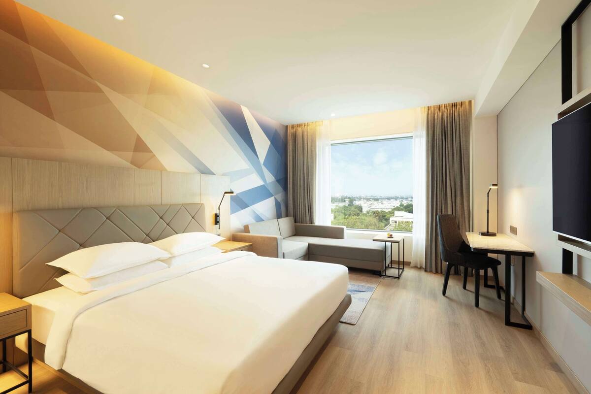 A hotel room with a large bed, a sofa, a desk, and a TV.