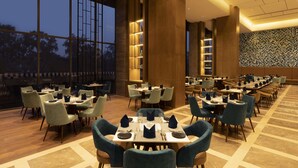 A spacious restaurant with multiple dining tables and chairs, large windows, and a modern interior design. - Hyatt Place Bharuch (Bharuch)